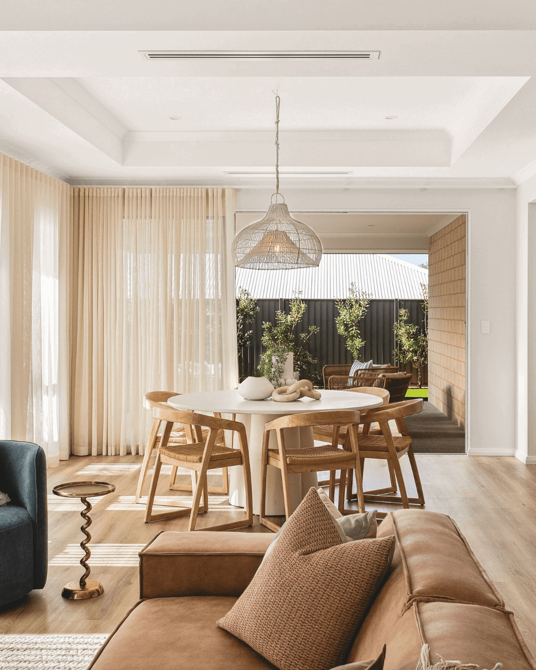 Bright and airy open-plan living room featuring a dining area with wooden chairs, a cozy sofa, and large windows with sheer curtains, perfect for contemporary Australian homes.