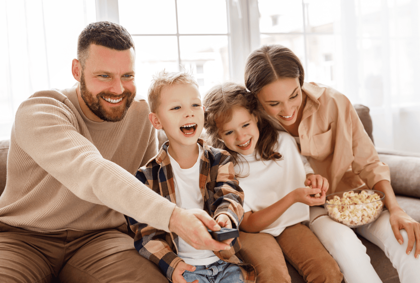 Happy family with two children watching a movie together on a sofa in a bright, cozy living room, showcasing a warm and inviting home environment.