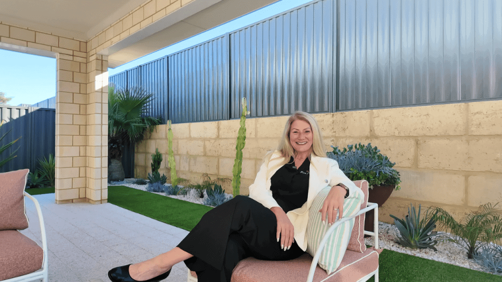 Smiling woman sitting on outdoor chair in a modern Perth home garden with lush plants and a brick wall, showcasing contemporary outdoor living space.